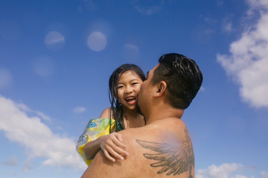 tattooed dad holds daughter in the water during hawaii family photos