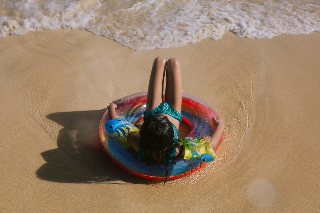 girl sitting in a rainbow float at kailua beach as waves wash in