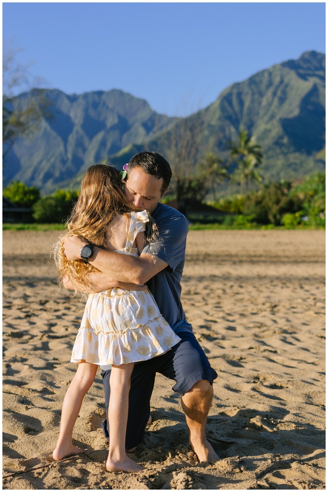 dad hugs daughter at the beach in hawaii with mountains beyond