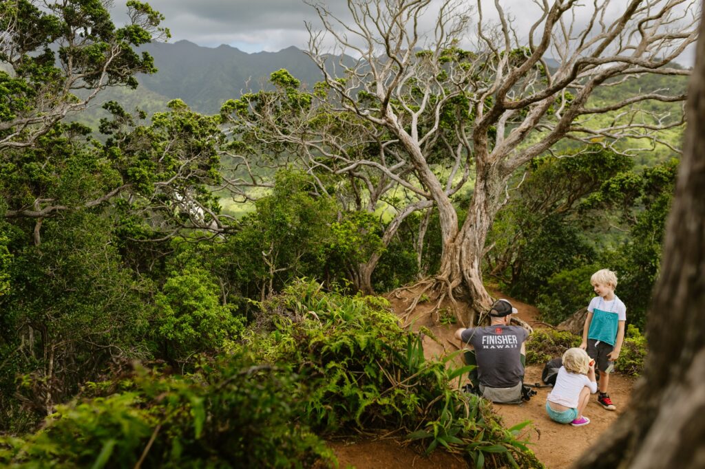 family takes a snack break on the aiea ridge tail with views of mountains beyond