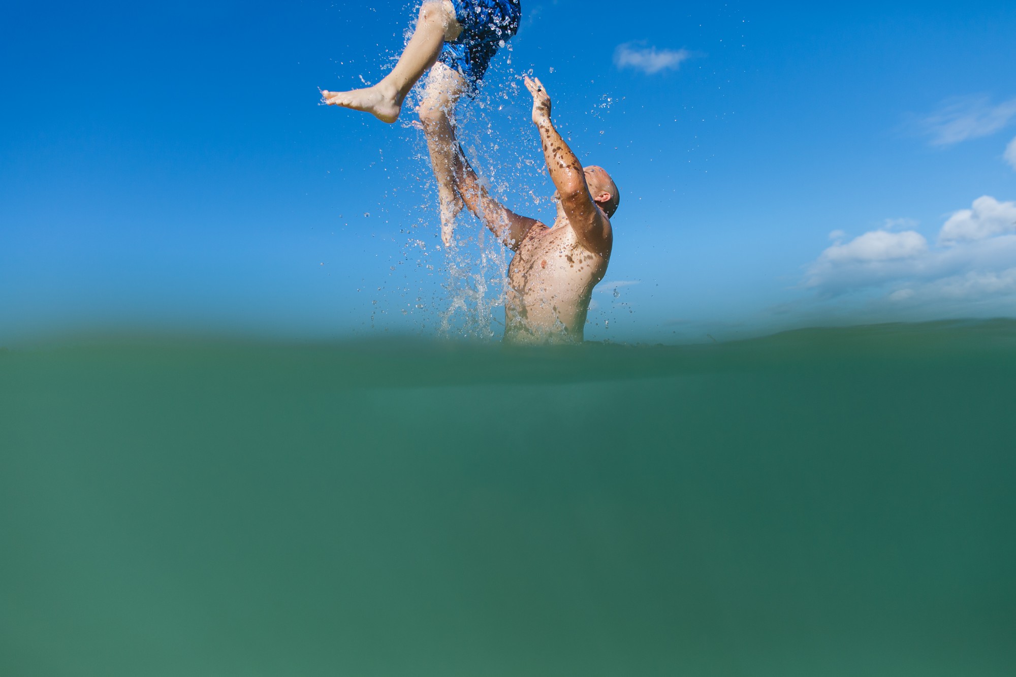 dad throwing son in clear blue water at paradise cove koolina