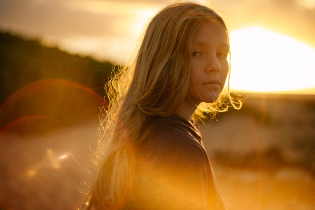 portrait of a girl at sandy beach at sunrise with sunflare