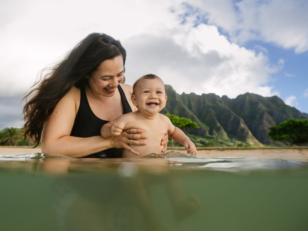 mom and baby play in the water with koolau mountains behind at kualoa beach park
