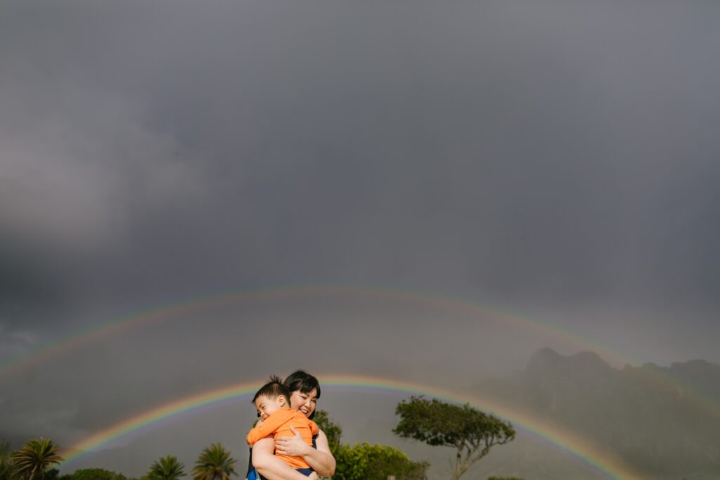 mom and sun hug under a rainbow at kualoa regional park