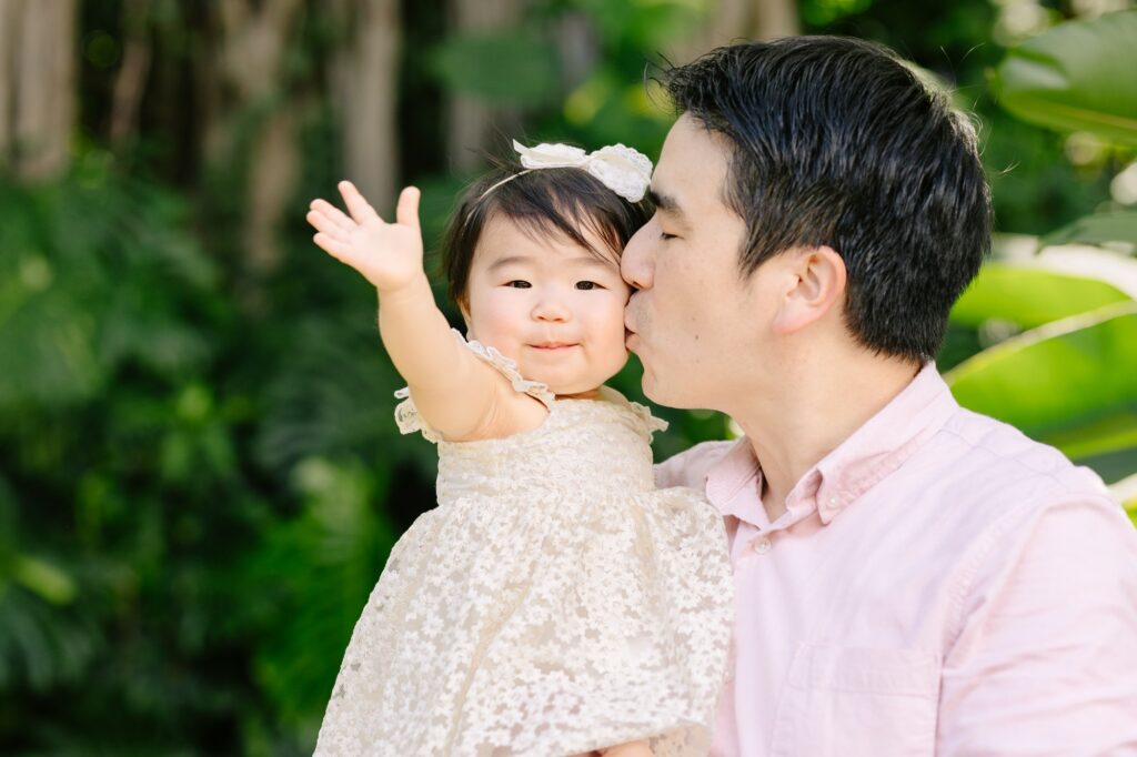 dad kissing baby daughter on the cheek while she waves