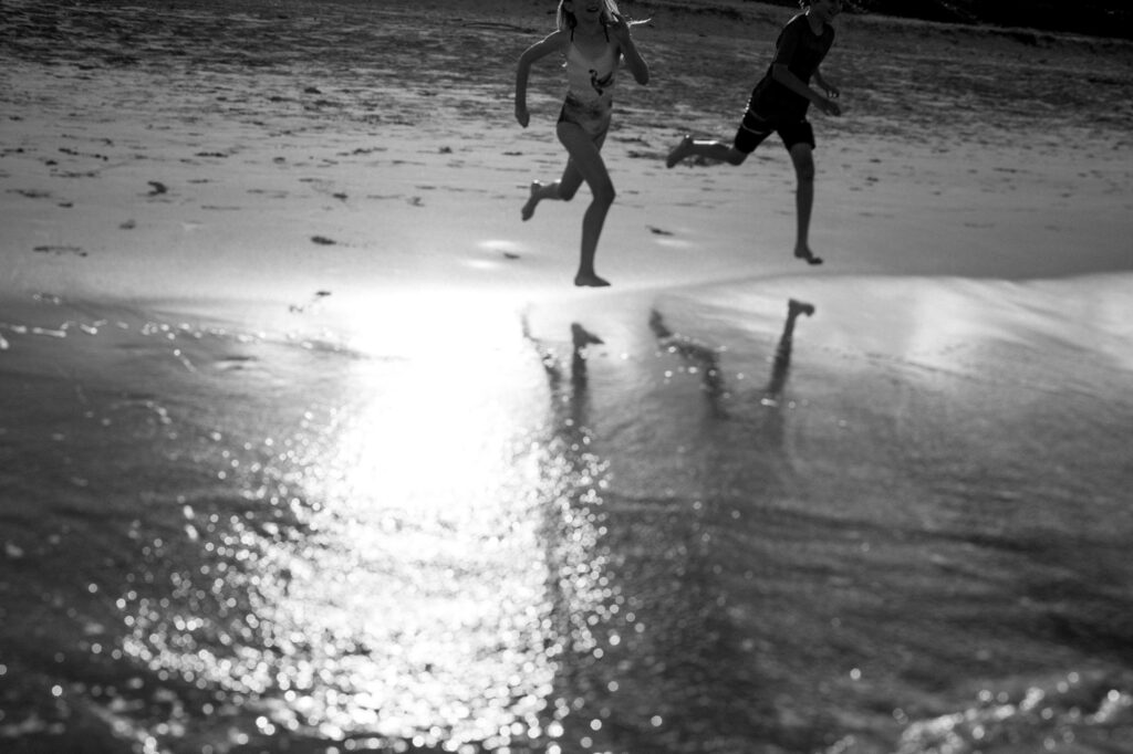 black and white portrait of siblings running towards the ocean at kailua beach oahu