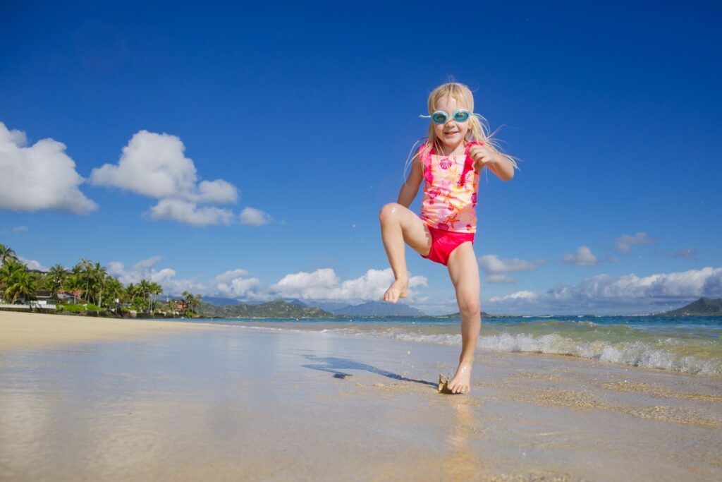 girl in a pink swimsuit with goggles against a bright blue sky at a hawaii beach