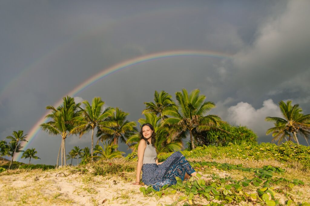 senior girl in Kailua sitting in the dunes with rainbow behind