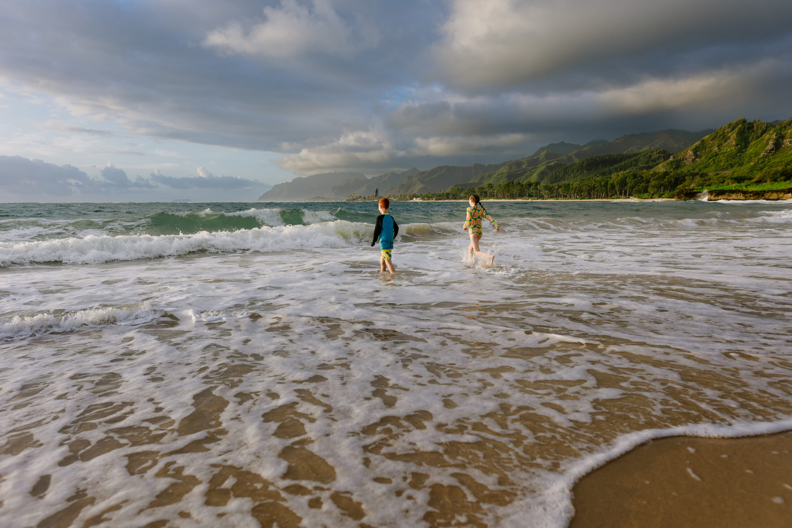 kids play in the water at laie beach park with mountains in the distance