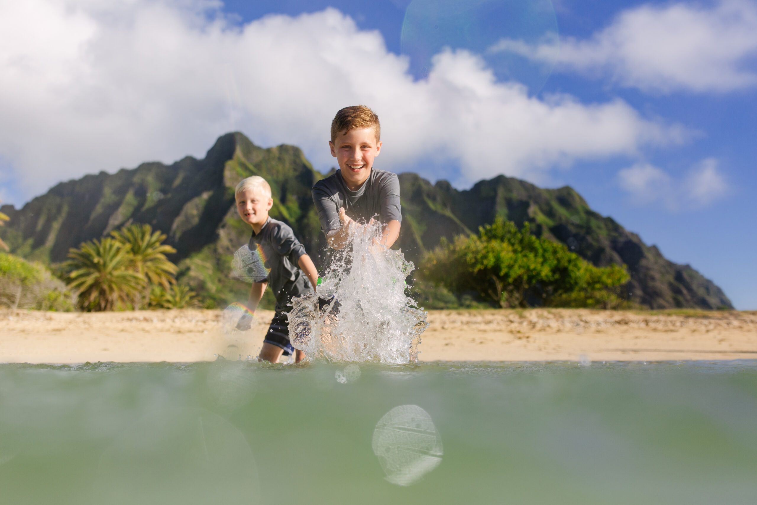 brothers splashing water with kualoa mountains in the distance