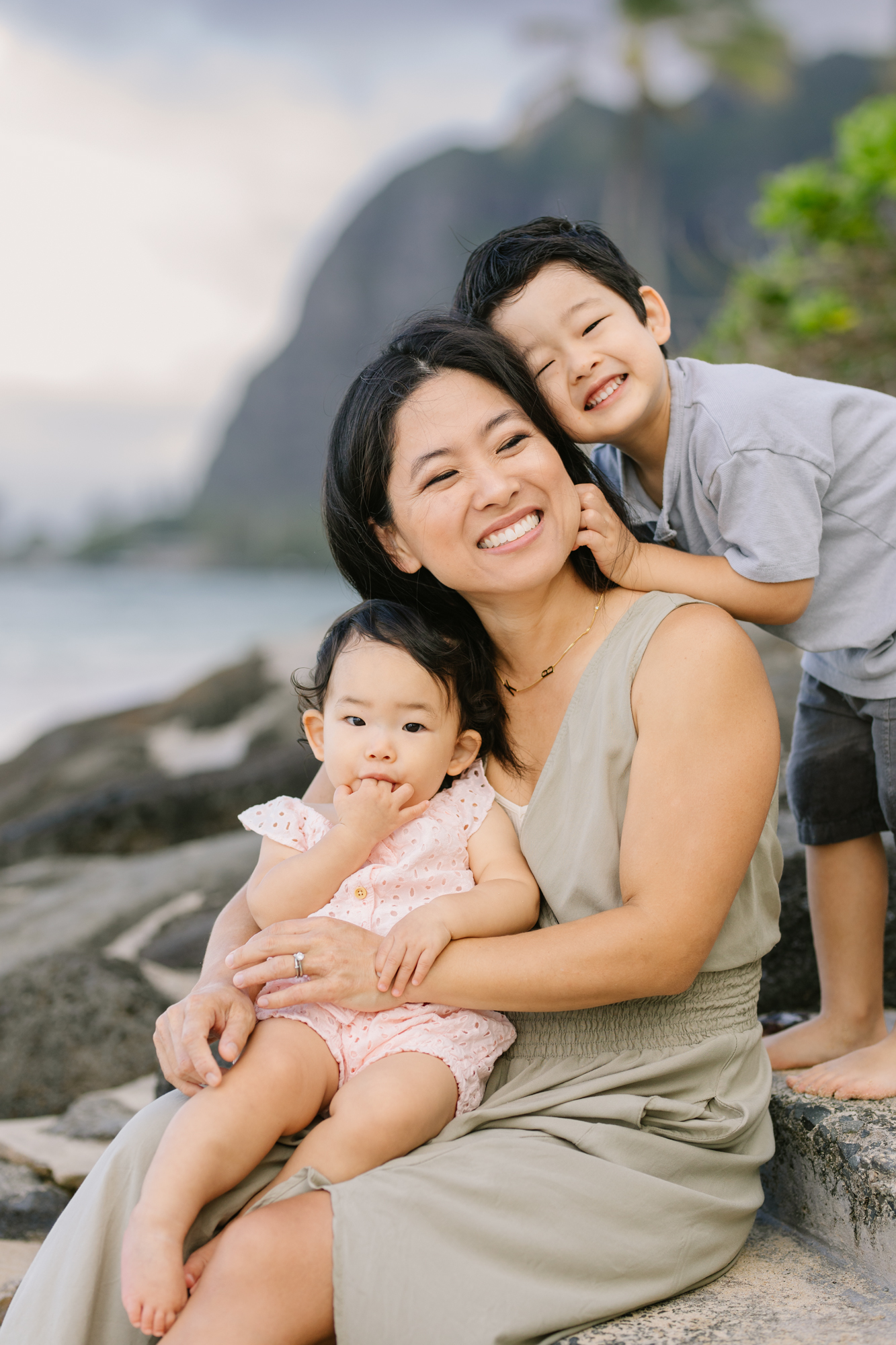 mom snuggling kids at the beach in hawaii with mountains behind