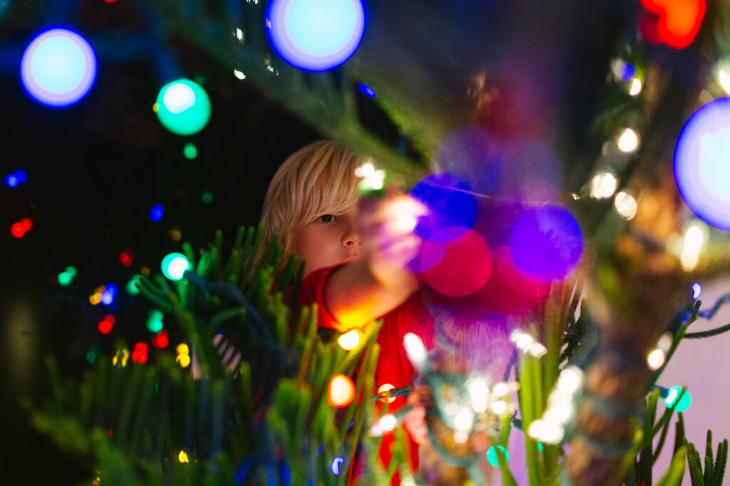 boy hanging ornaments in a christmas tree with colorful lights