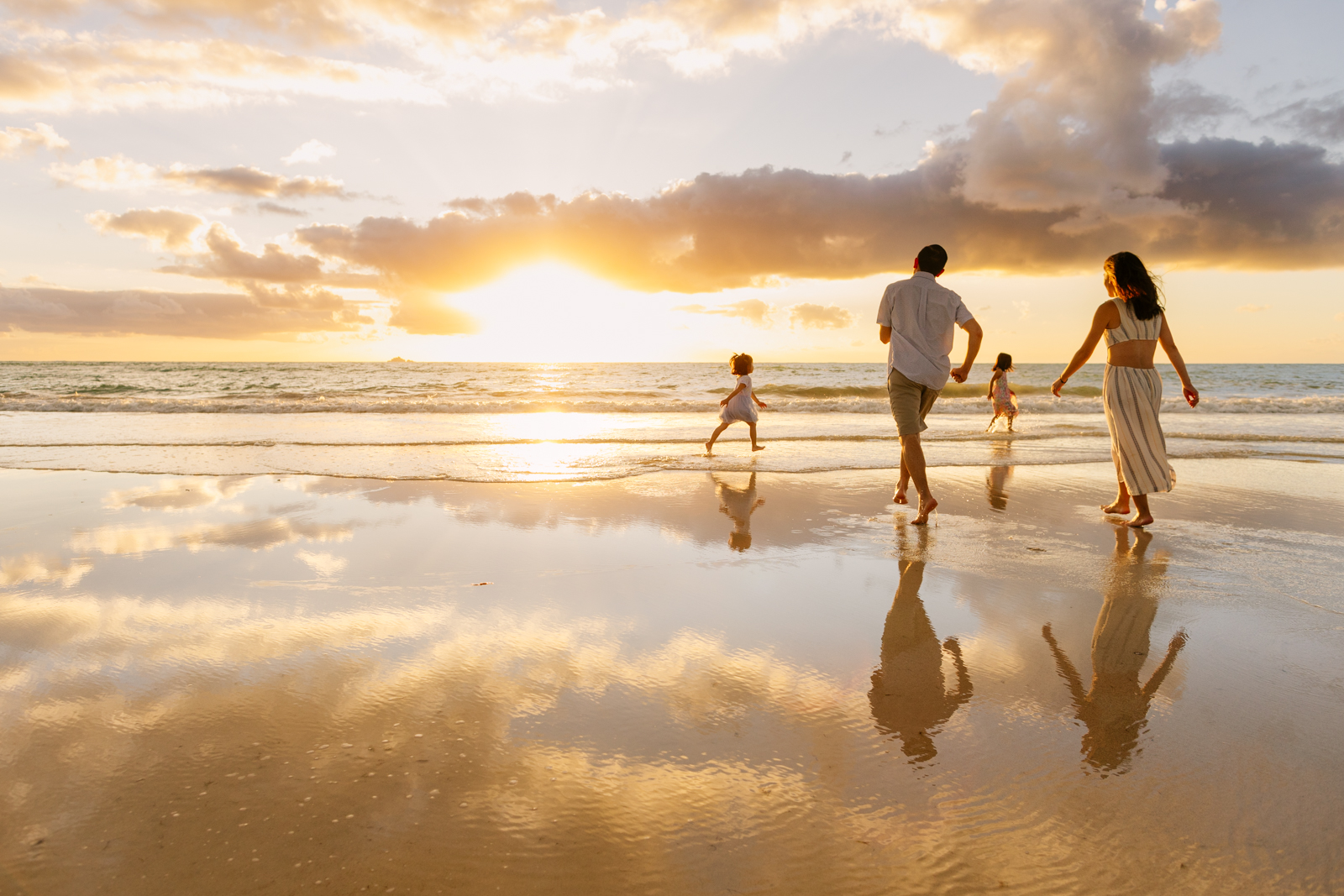 a family of 4 runs along kailua beach at sunrise with water reflecting the sky