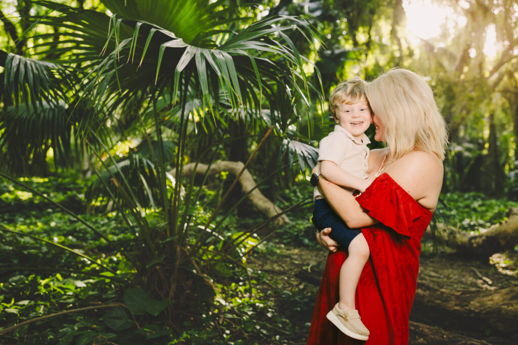 mom and toddler son laugh and hug against a tropical background in maui