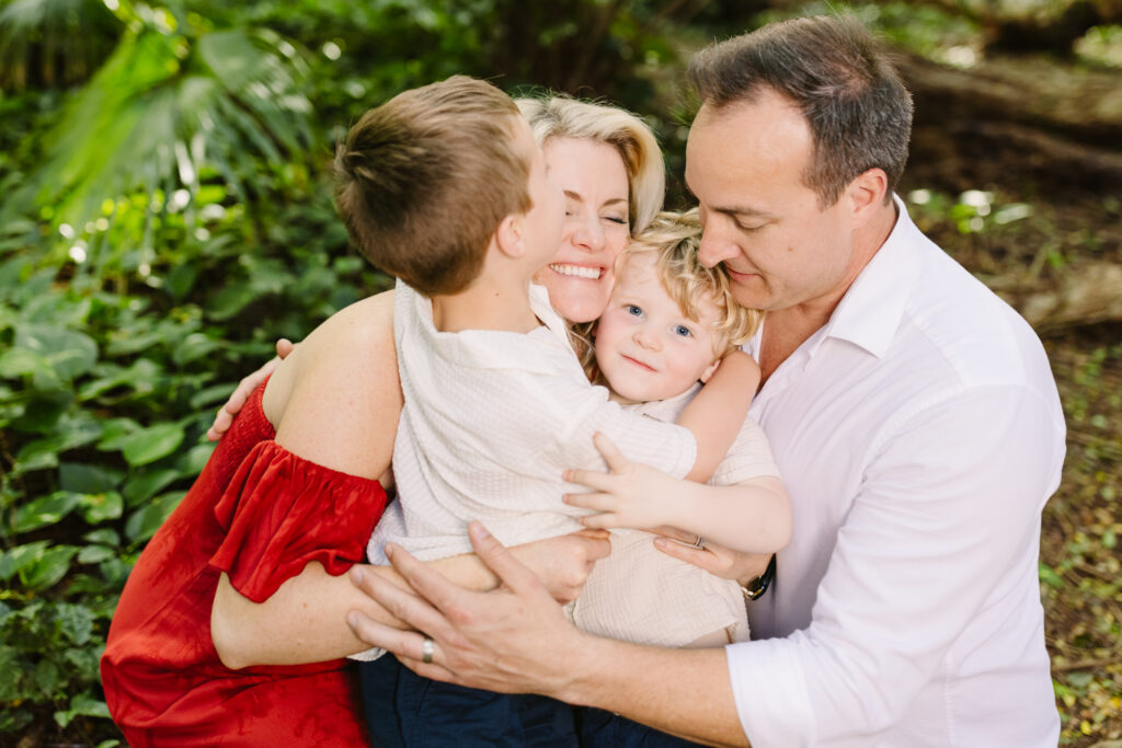 family of 4 hug with toddler looking at camera