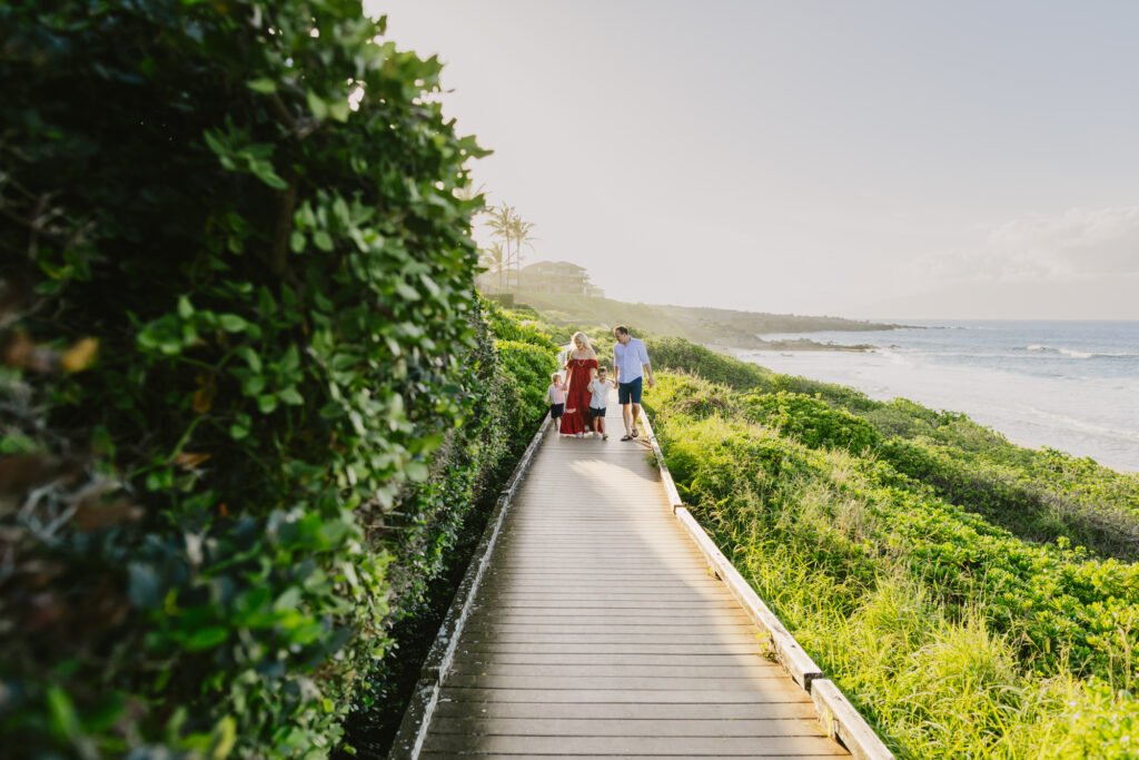 family of 4 walks along the boardwalk at ironwoods beach on maui