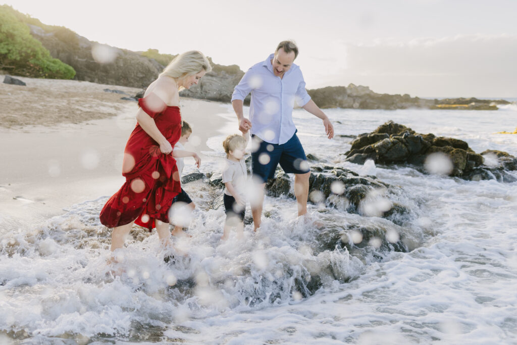 waves splash a family at sunset during maui family photos