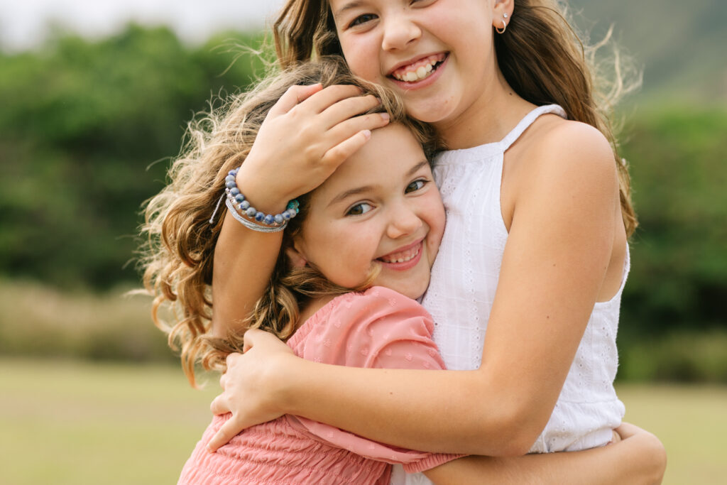 sisters hug at kualoa beach on windward oahu for vacation family photography Hawaii