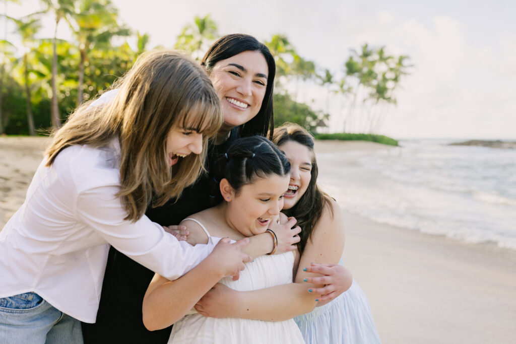 a mom shares a big hug with her daughters on the beach at ko olina