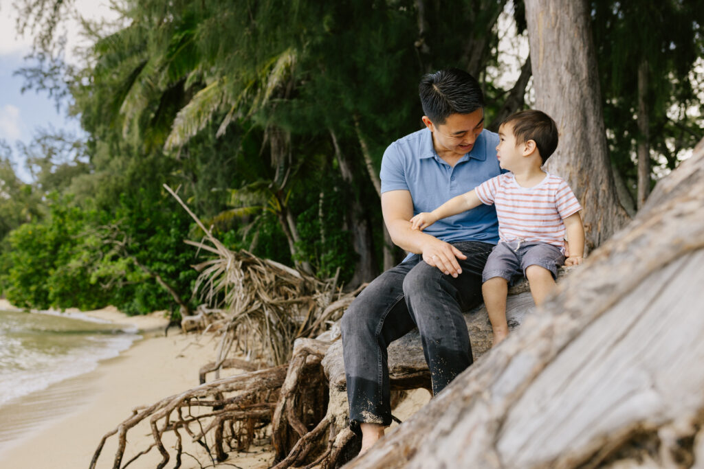 a dad and toddler son sit on a long on the north shore for family photos with toddlers Hawaii